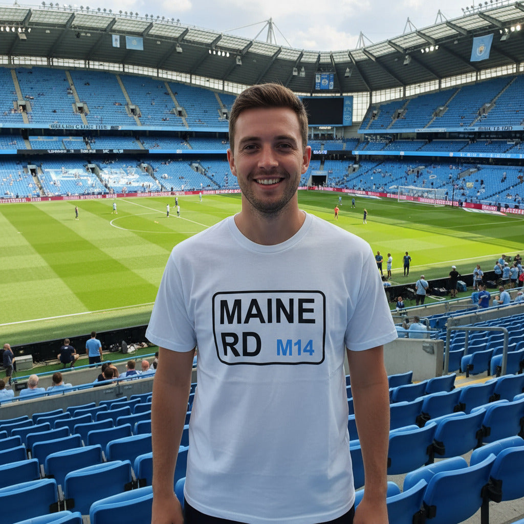 Man wearing a white t-shirt with 'MAINE RD M14' text at a sports stadium.