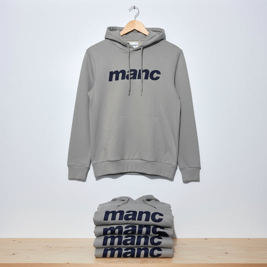 Grey manc hoodie on a wooden hanger with more on a wooden shelf below it.