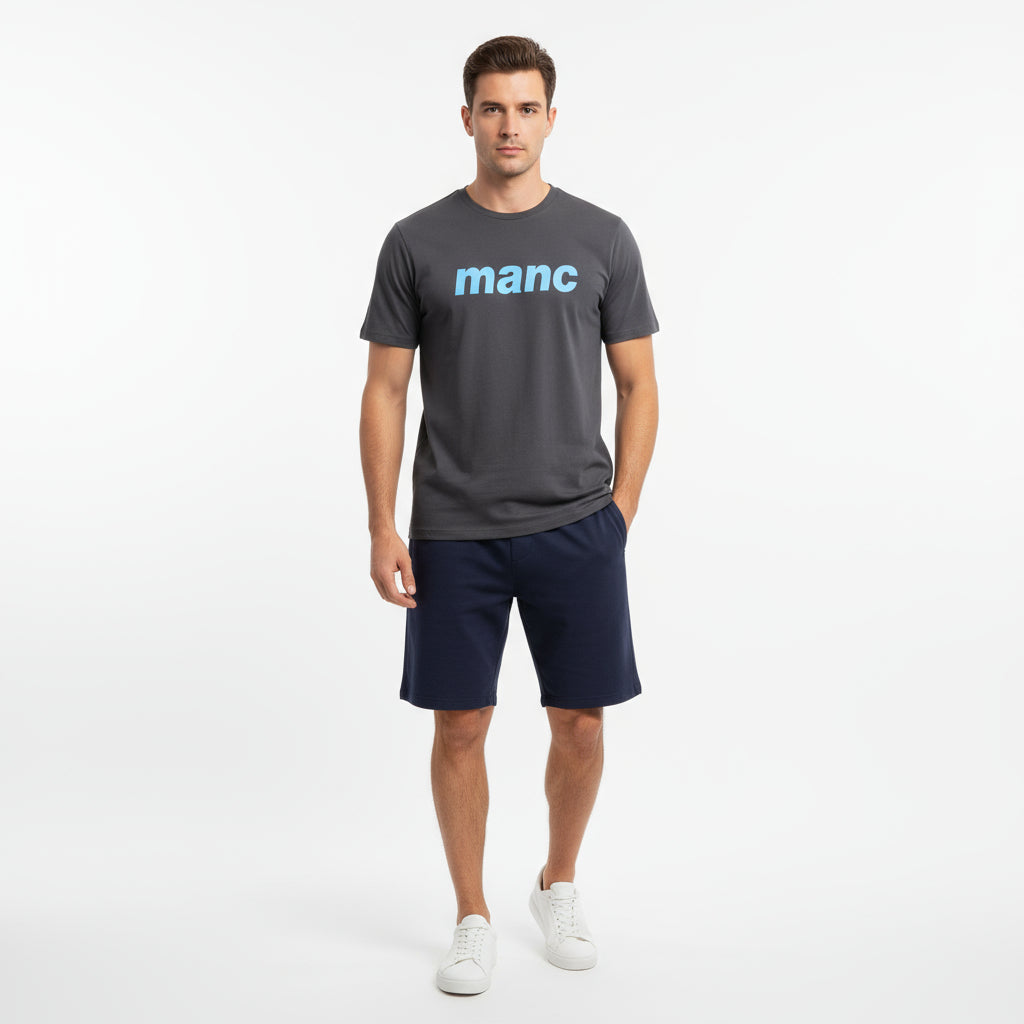 Man wearing a dark grey manc t-shirt and navy shorts against a white background