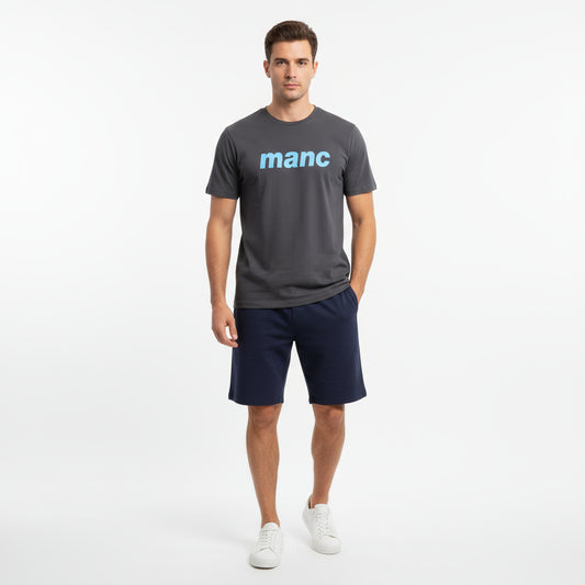 Man wearing a dark grey manc t-shirt and navy shorts against a white background