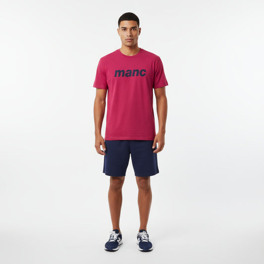 Man wearing a red manc t-shirt and navy shorts on a white background