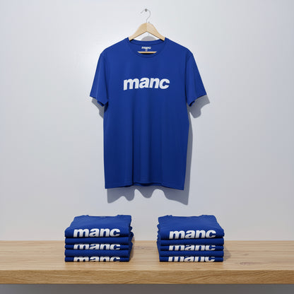 Blue t-shirt with 'manc' text on a hanger and stacked below against a white wall.