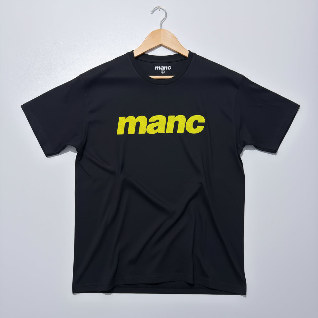 black t-shirt with the word 'manc' written on it in a yellow puff vinyl against a white backdrop