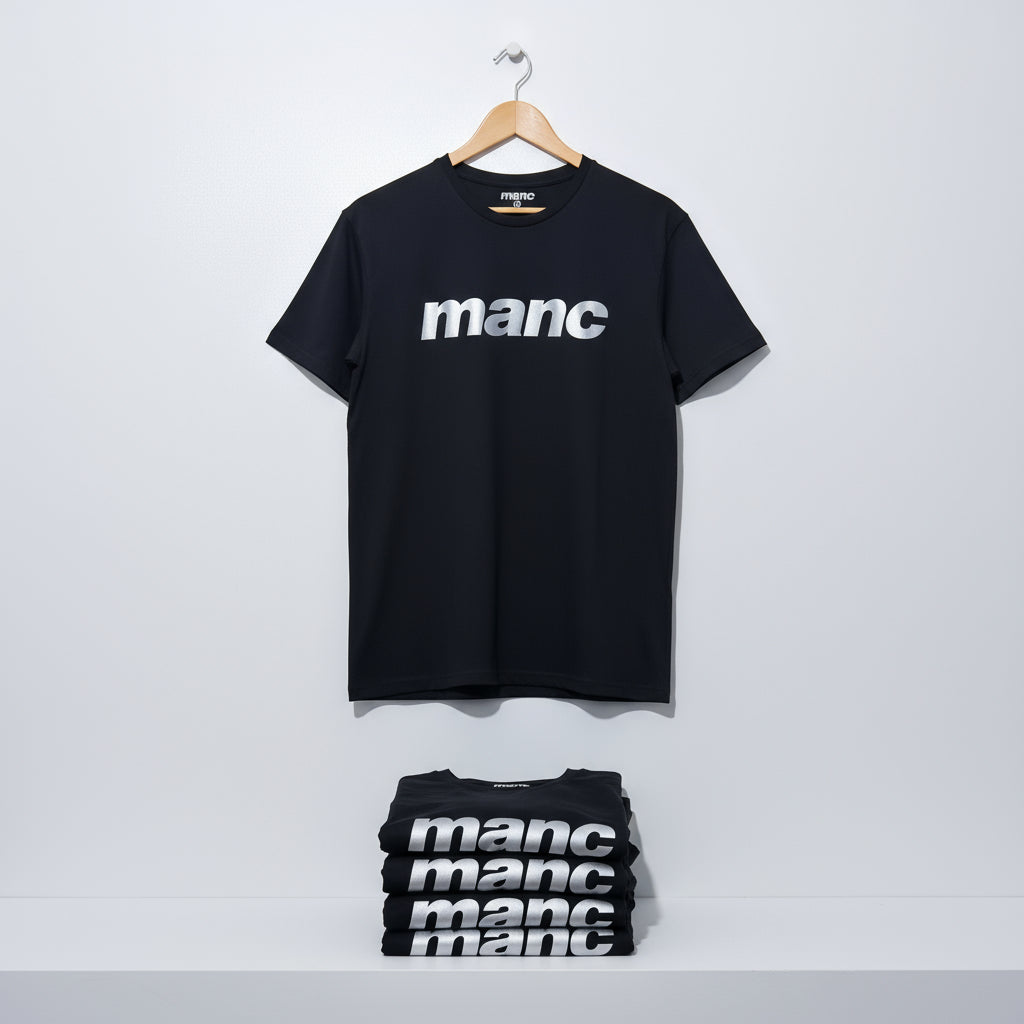 Black t-shirt with 'manc' text in reflective vinyl on a hanger against a white background