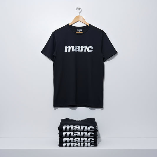 Black t-shirt with 'manc' text in reflective vinyl on a hanger against a white background