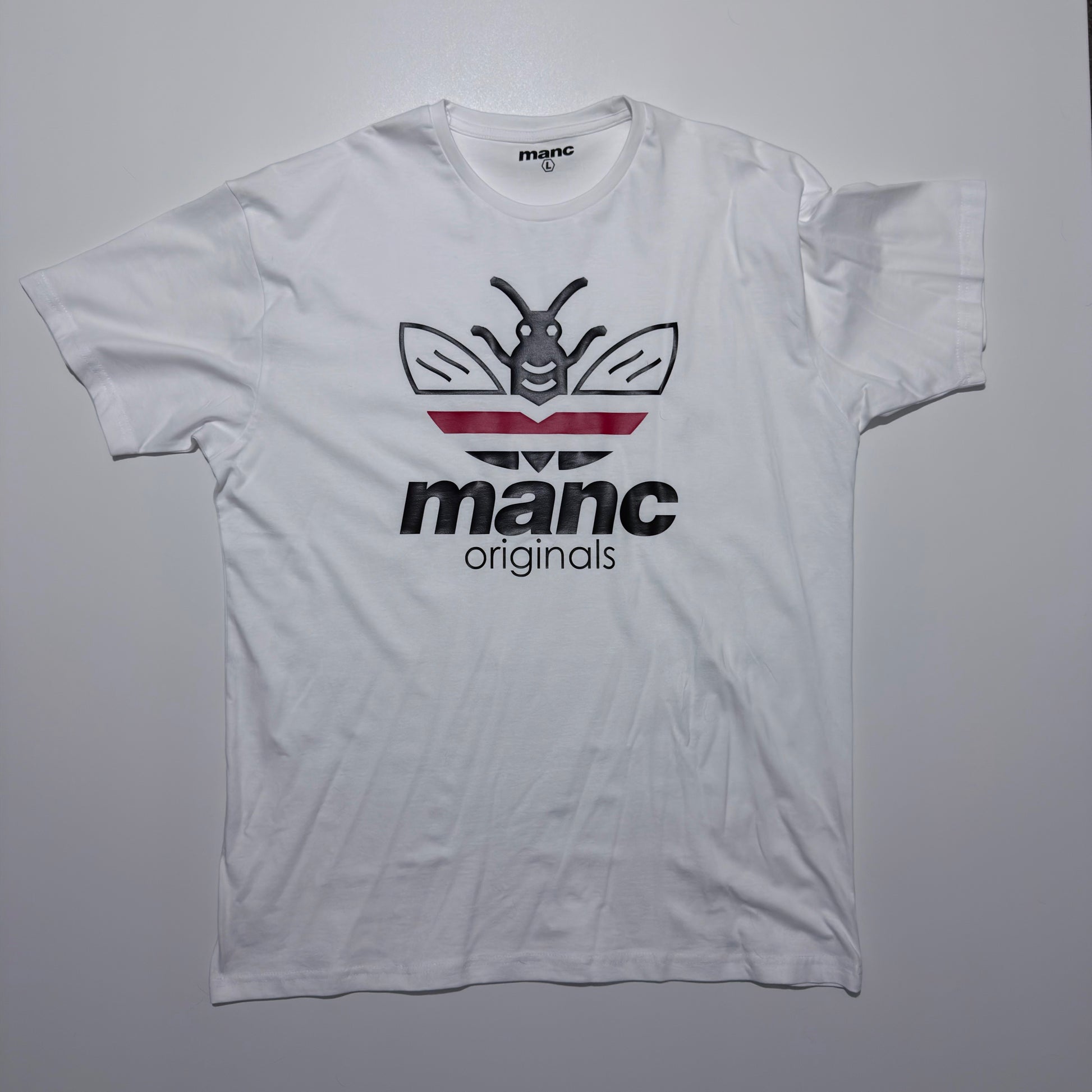 White t-shirt with 'manc originals' logo on a grey background