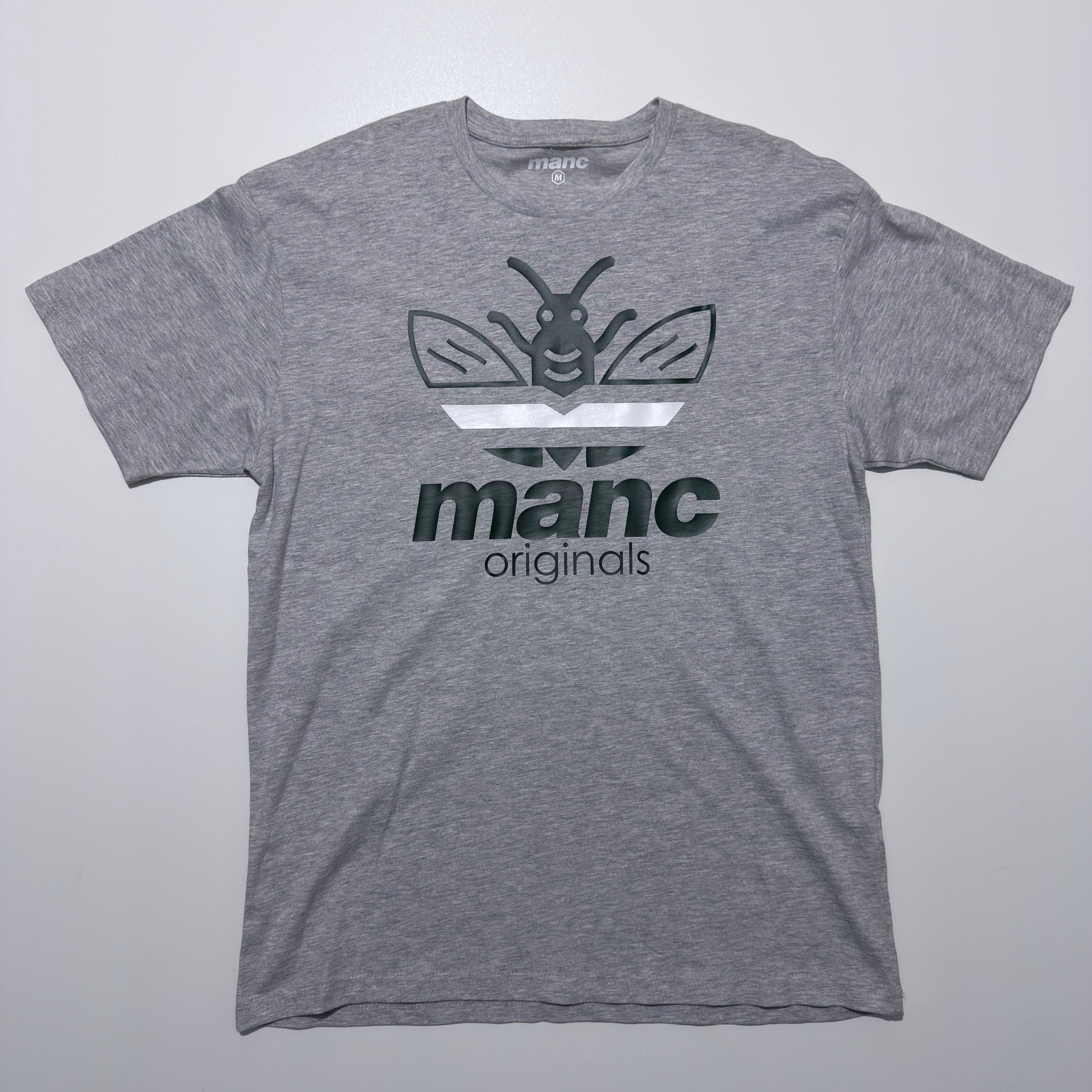 Grey t-shirt with a manc originals logo and text on a light grey background