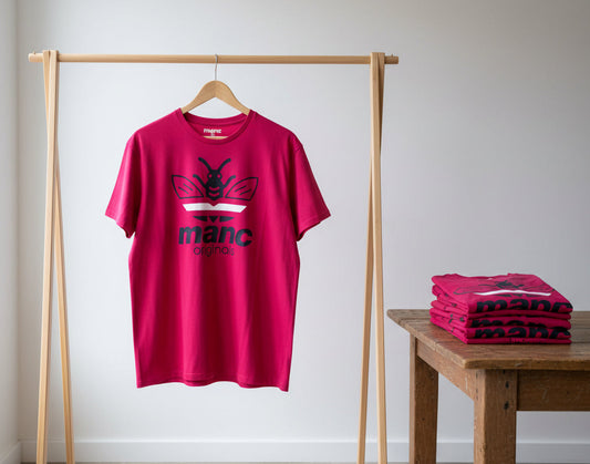 Red t-shirt with a 'manc originals' logo on a wooden rack and table against a white wall
